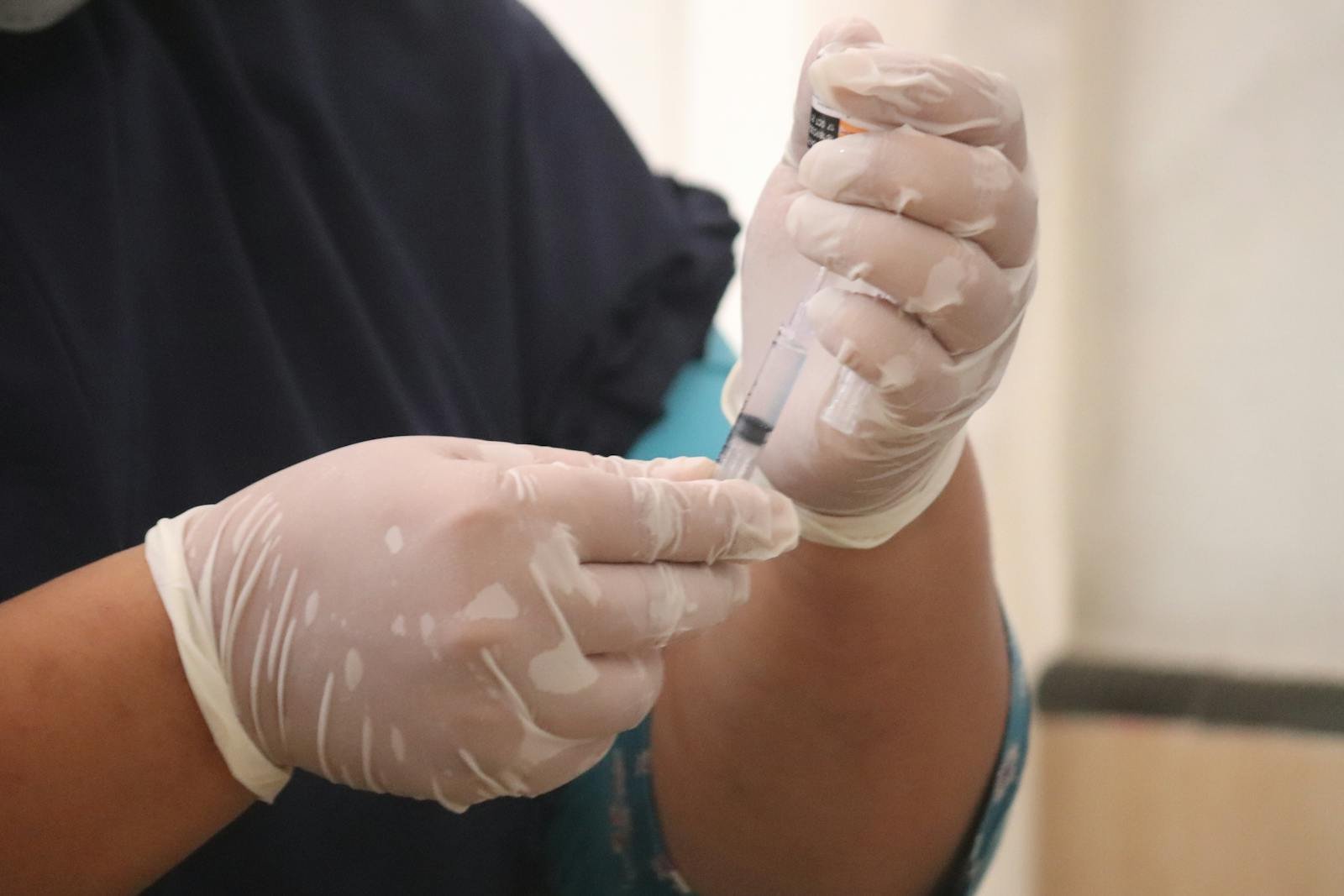 Close-up of hands wearing latex gloves preparing a syringe in a medical setting.